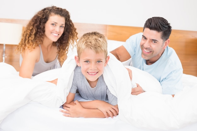 Linda familia joven sonriendo a la cámara en la cama