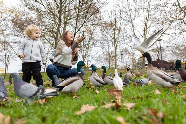 Una linda familia de madre y su pequeño hijo en el parque rodeados de palomas y patos