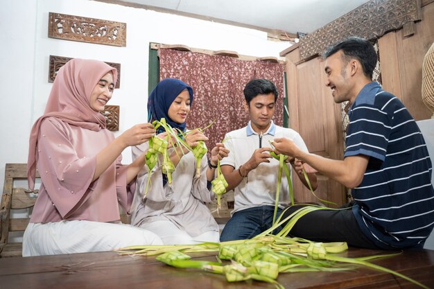 Linda família muçulmana e amiga fazendo bolo de arroz de ketupat em casa usando folha de palmeira para a tradição de eid fitr mubarak