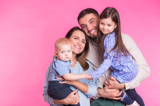 Linda familia posando y sonriendo a la cámara juntos sobre fondo rosa