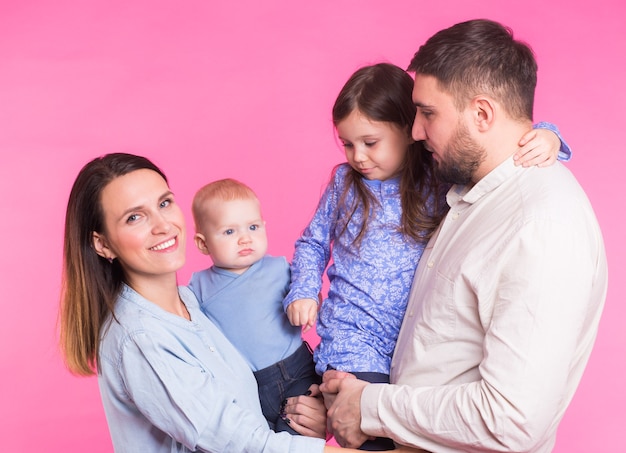 Linda familia posando y sonriendo a la cámara juntos sobre fondo rosa