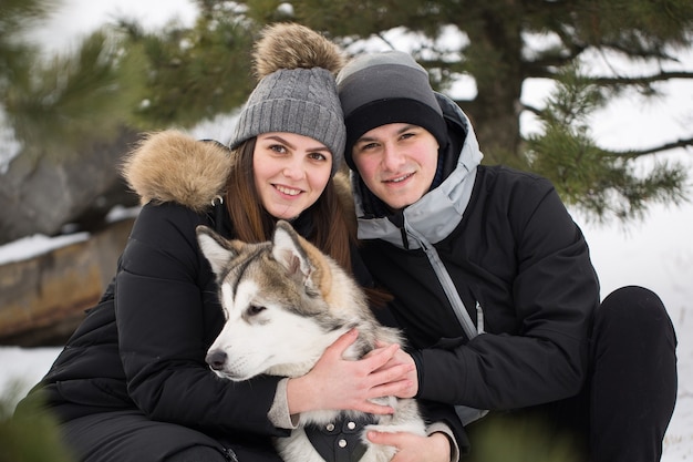 Linda família, um homem e uma garota na floresta de inverno com o cachorro. Brinque com o cão husky siberiano.