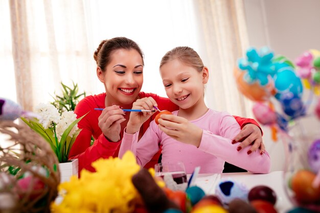 Linda felicidade mãe e filha pintando ovo de páscoa em casa.