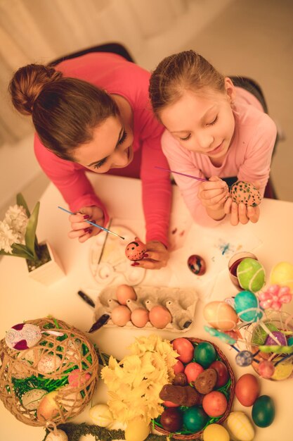 Foto linda felicidade mãe e filha pintando ovo de páscoa em casa.