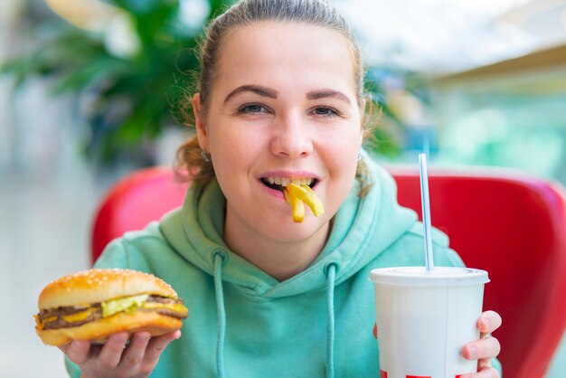 Linda feliz alegre jovem positiva sentada na praça de alimentação em um shopping, segurando