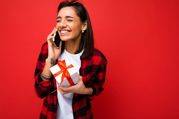 Linda feliz emocional jovem morena feminina isolada sobre uma parede de fundo vermelho usando