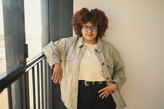 Linda, feliz, sorridente, curvilínea plus size, negra africana, cabelo afro, posar, camiseta jeans bege