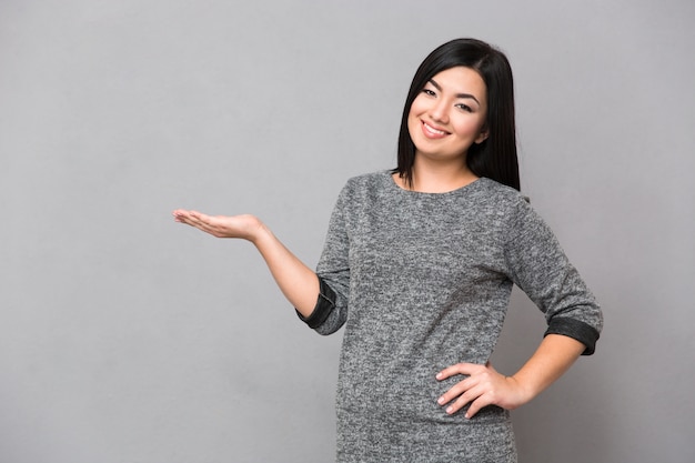 Linda feliz sorridente mulher asiática em um macacão cinza olhando para a frente segurando copyspace na palma da mão