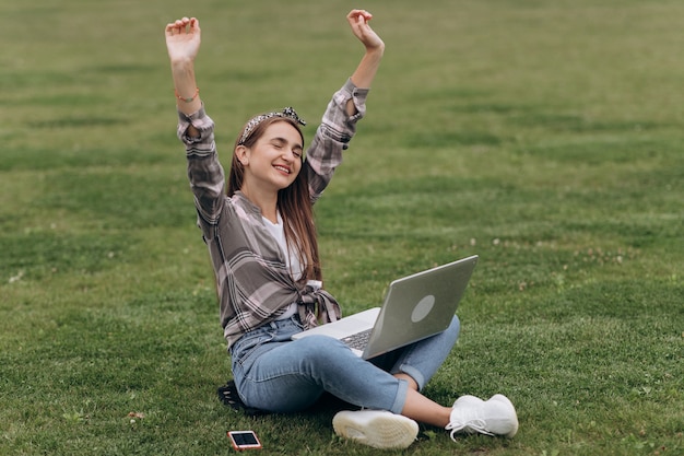 Linda fêmea casual sentado na grama, usando o laptop. Retrato de mulher jovem e atraente sentado na grama verde no parque