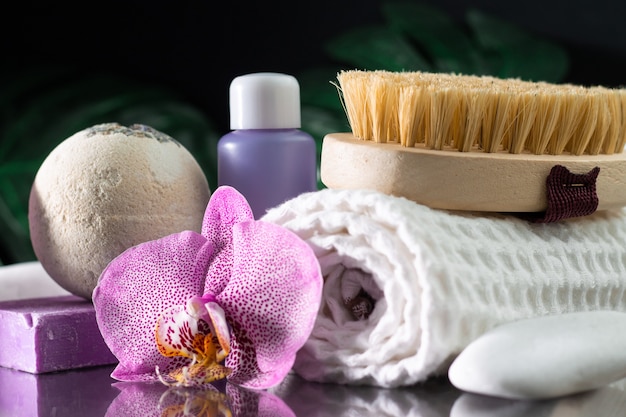 Linda flor de orquídea lilás, frasco de cosmético, escova de massagem, toalha enrolada e sabonete artesanal com pedra branca e folhas de monstera