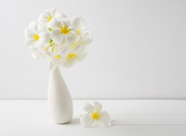 Foto linda flor de spa frangipani em um vaso de cerâmica branco moderno na mesa de madeira, superfície de parede branca com espaço de cópia