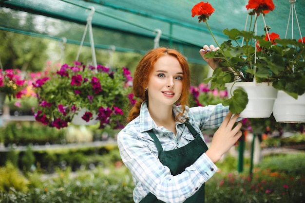 Linda florista de avental trabalhando com flores. Jovem de pé com flores e olhando sonhadoramente na câmera