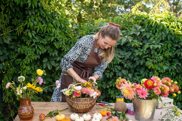 Linda florista recoge un ramo de flores de otoño en una cesta