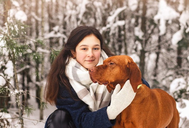 Linda garota abraça o cachorro em uma caminhada na floresta de inverno