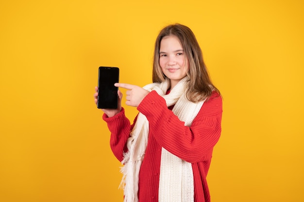 Linda garota adolescente apontando o dedo para o telefone com espaço em branco isolado em fundo amarelo