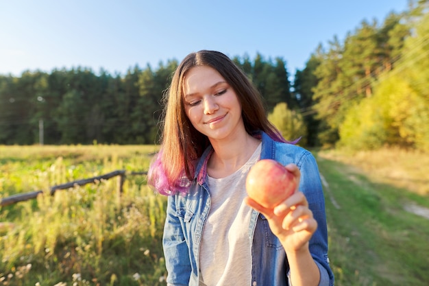Linda garota adolescente com maçã vermelha, jovem feliz na natureza, fundo de paisagem do pôr do sol cênico, espaço de cópia, conceito de comida natural saudável