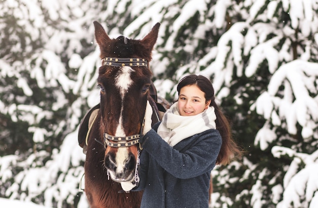 Linda garota adolescente com um cavalo no inverno na floresta. Comunicando-se com animais