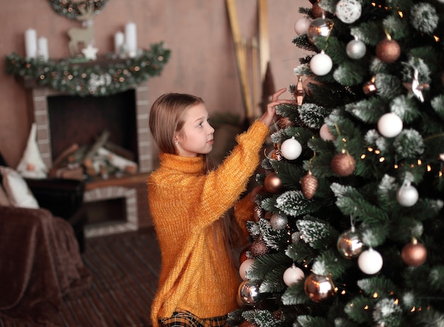 Linda garota adolescente decorando a árvore de natal na sala de estar dela. o conceito de natal