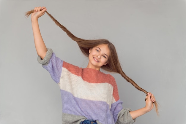 Linda garota adolescente feliz com sardas brilhantes no rosto e aparelho segurando o cabelo e sorrindo