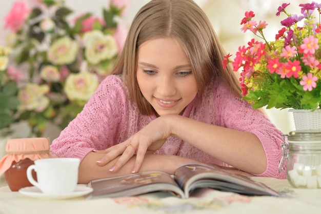 Linda garota adolescente lendo revista em casa com chá