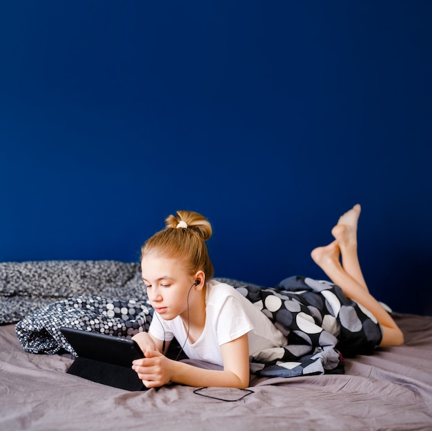 Linda garota adolescente loira assistindo vídeo sobre tablet na cama