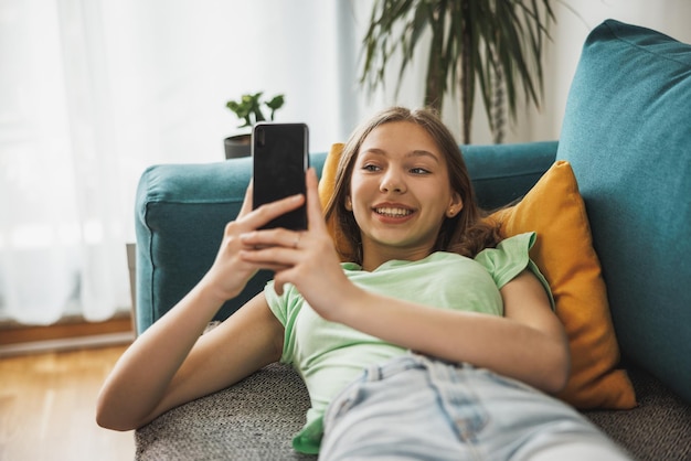 Linda garota adolescente surfando nas mídias sociais no telefone inteligente enquanto tem tempo de lazer em sua casa.