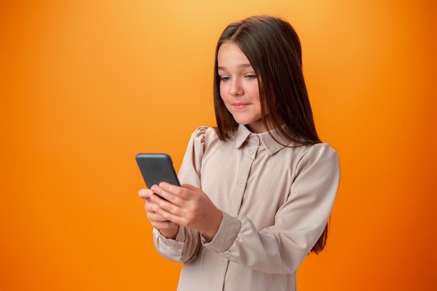 Linda garota adolescente usando telefone celular com expressão positiva contra fundo laranja