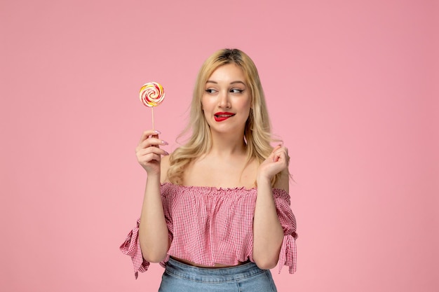 Linda garota adorável jovem com batom vermelho na blusa rosa segurando pirulito mordendo os lábios