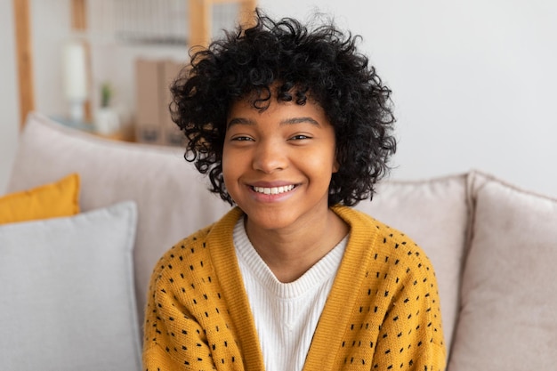 Linda garota afro-americana com penteado afro sorrindo sentada no sofá em casa jovem interior afr