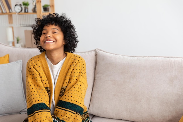 Linda garota afro-americana com penteado afro sorrindo sentada no sofá em casa jovem interior afr