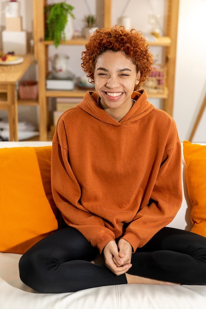 Linda garota afro-americana com penteado afro sorrindo sentada no sofá em casa jovem interior afr