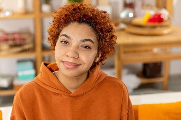 Linda garota afro-americana com penteado afro sorrindo sentada no sofá em casa jovem interior afr