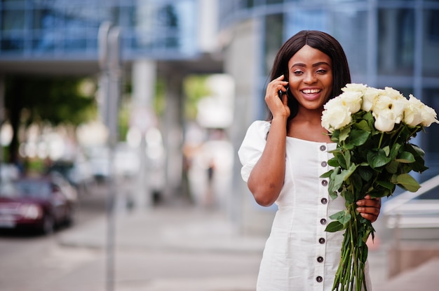 Linda garota afro-americana em um vestido branco com flores nas mãos