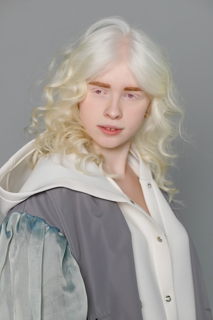 Linda garota albina com pele branca, lábios naturais e cabelo branco encaracolado, vestindo uma camisola branca elegante, foto de close-up, espaço de cópia, beleza, moda. Menina loira