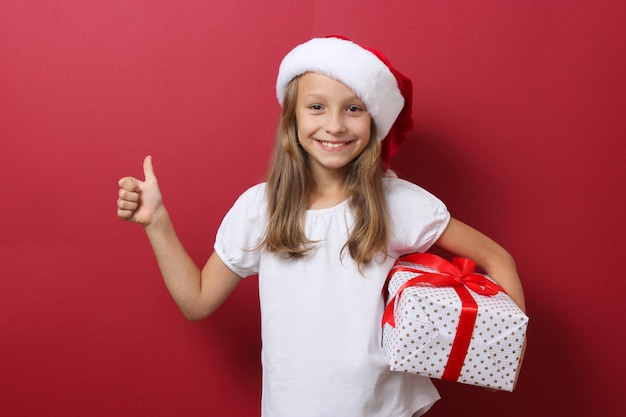 Linda garota alegre com um chapéu de Natal em um fundo colorido segurando um presente