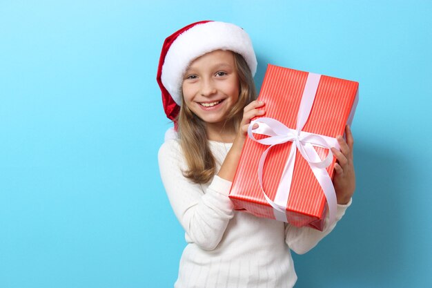 Linda garota alegre com um chapéu de Natal em um fundo colorido segurando um presente