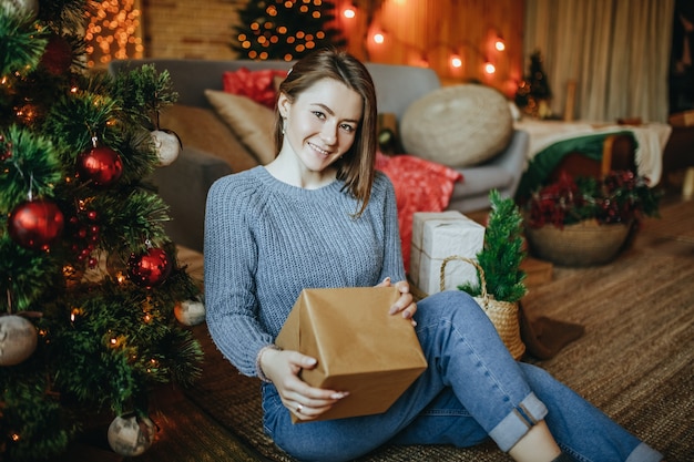 Linda garota alegre e feliz com presentes de natal no chão perto da árvore de ano novo em casa