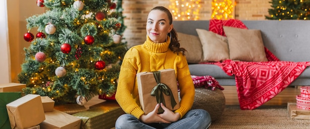 Linda garota alegre e feliz com presentes de Natal no fundo de uma árvore de ano novo em casa