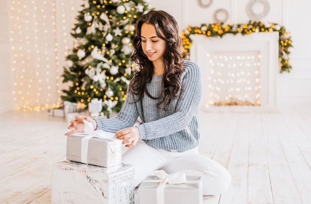 Linda garota alegre e feliz com presentes de natal no fundo de uma árvore de ano novo em casa