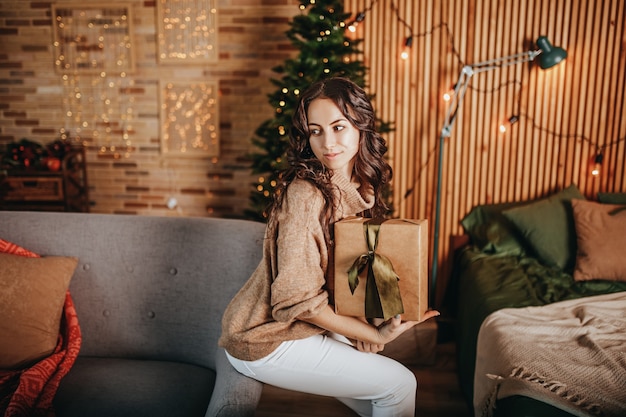 Linda garota alegre e feliz com presentes de Natal no sofá no fundo de uma árvore de ano novo em casa