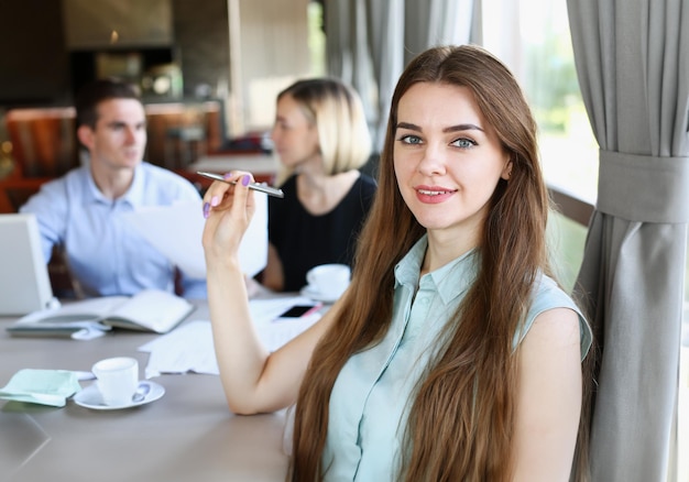 Linda garota alegre sorridente no café olha na câmera com o grupo de colegas no fundo Trabalhador de colarinho branco no trabalho no espaço de trabalho oferece estilo de vida moderno cliente visita profissão trem conceito