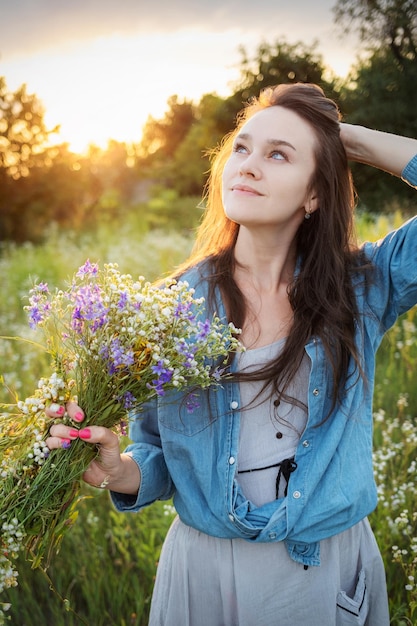 Linda garota andando no campo no verão com flores silvestres