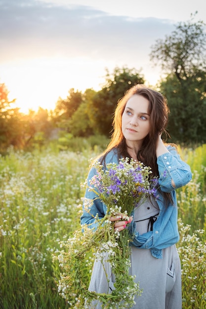 Linda garota andando no campo no verão com flores silvestres