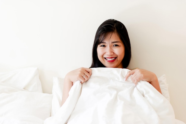 Linda garota asiática acordando na cama no quarto branco Sorria brilhantemente pela manhã