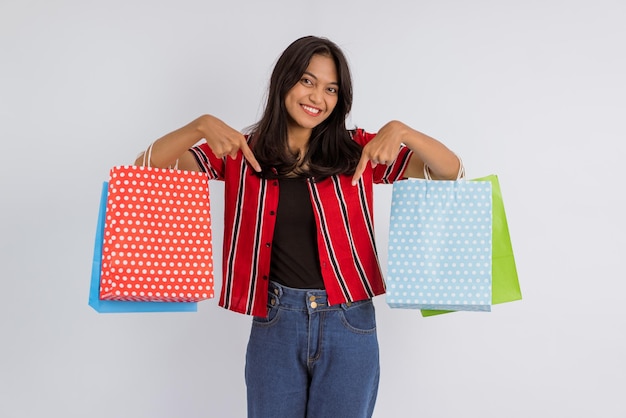 Linda garota asiática apontando para cima enquanto traz as sacolas de compras em fundo isolado
