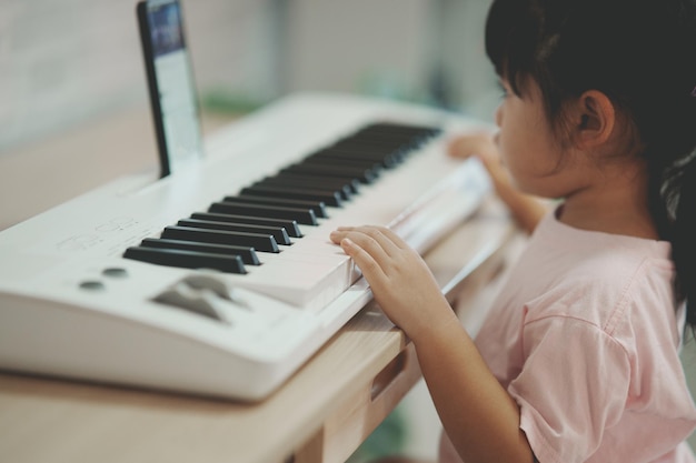 Linda garota asiática aprendendo música de piano online com professor por celular ou tablet A ideia de atividades para a criança em casa durante a quarentena Conceito de estudo online de aprendizagem de música