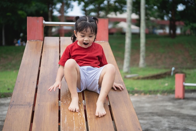 Linda garota asiática brinca na escola ou jardim de infância ou playground Atividade saudável de verão para crianças Menina asiática escalando ao ar livre no playground Criança brincando no playground ao ar livre