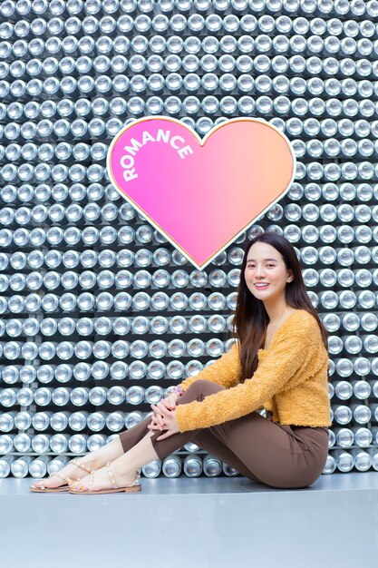 Linda garota asiática com cabelo comprido está sentada e sorrindo no fundo do coração como dia dos namorados