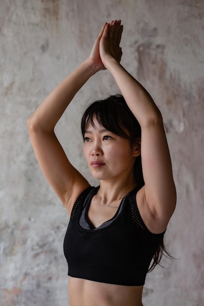 linda garota asiática com cabelos longos escuros em leggings esportivas de treino e top fazendo ioga