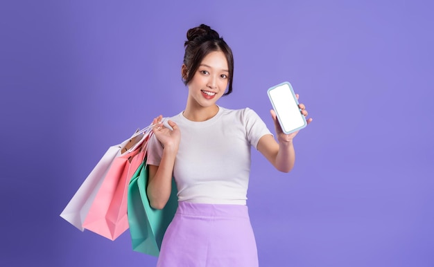 Linda garota asiática segurando sacola de compras posando em fundo roxo